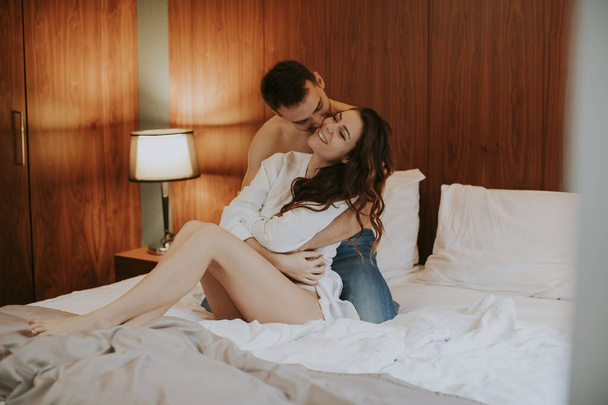 Loving and hugged young couple sitting on the bed in the bedroom - Photo, Image