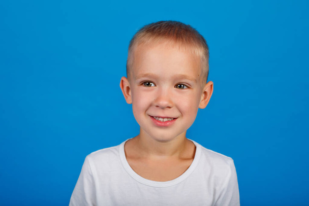 Retrato de un niño feliz. Un niño con una camiseta blanca sobre un fondo azul - Foto, Imagen