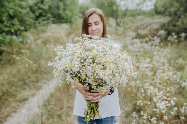 Beautiful girl embracing bouquet of white gypsophila on the green meadow. Selective focus in flowers - Photo, Image