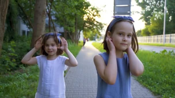Két aranyos kislány sétál a város utcáin naplementekor. - Felvétel, videó