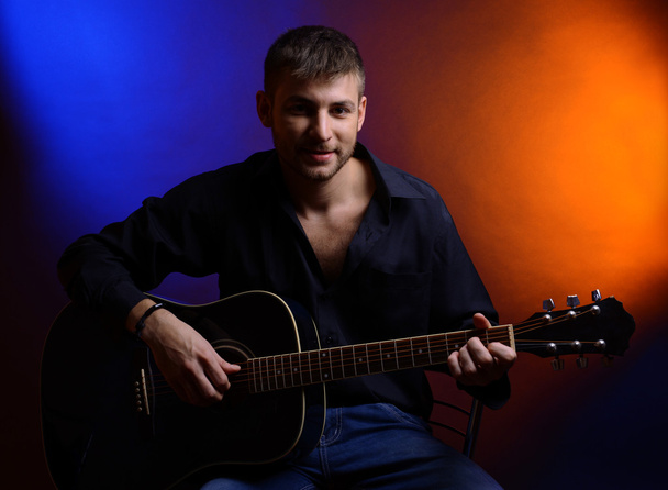 Young musician playing acoustic guitar and singing, on dark color background - Fotografie, Obrázek