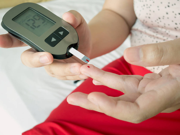 Asiatin misst Glukosespiegel mit digitalem Glukosemessgerät, Diabetes-Test - Foto, Bild