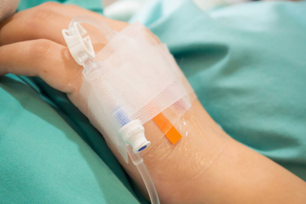 Ασιάτισσα ασθενής χέρι σε IV στάγδην με αλατούχο διάλυμα, θεραπεία υποκατάστασης υγρών - Φωτογραφία, εικόνα