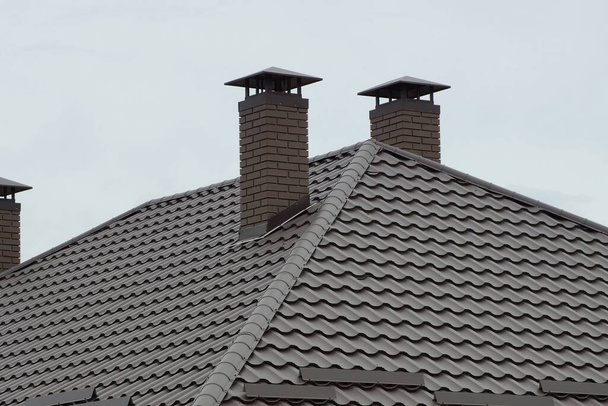 hnědá kachlová střecha soukromého domu s cihlovými komíny proti šedé obloze - Fotografie, Obrázek