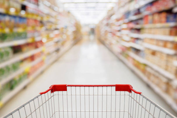 Shopping cart view in Supermarket aisle with product shelves abstract blur defocused background - Foto, immagini