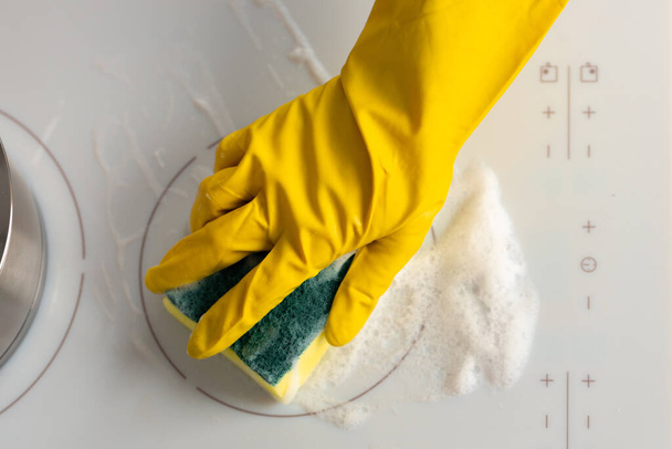Female hands in yellow gloves cleaning electrical stove with a sponge - Фото, изображение