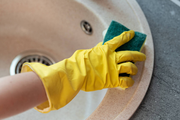 Hands in yellow gloves cleaning a sink with a sponge - Фото, зображення