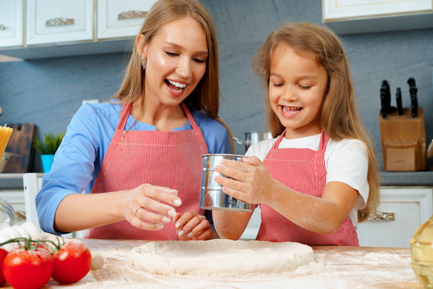Mother and her little daughter preparing dough in kitchen - Fotó, kép