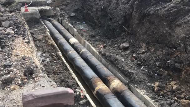 Open trench with pipes of the heating installation. Repair work on the sidewalk. Preparing for the heating season. Replacement of pipes in the heating system. People walk down the street - Footage, Video