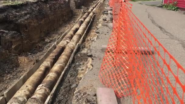 Open trench with pipes of the heating installation. Repair work on the sidewalk. Preparing for the heating season. Replacement of pipes in the heating system. People walk down the street - Footage, Video