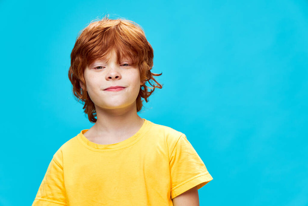 Улыбающийся мальчик с рыжими волосами в желтой футболке смотрит вперед  - Фото, изображение