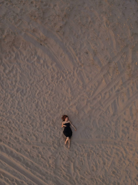 Young woman in a black dress lying on the back on the sand. Top view from the drone. Aerial Shooting. - Foto, Imagem