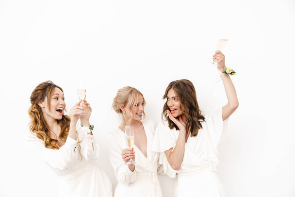 Photo of delighted young bridesmaids dancing and drinking champagne isolated over white wall - Zdjęcie, obraz