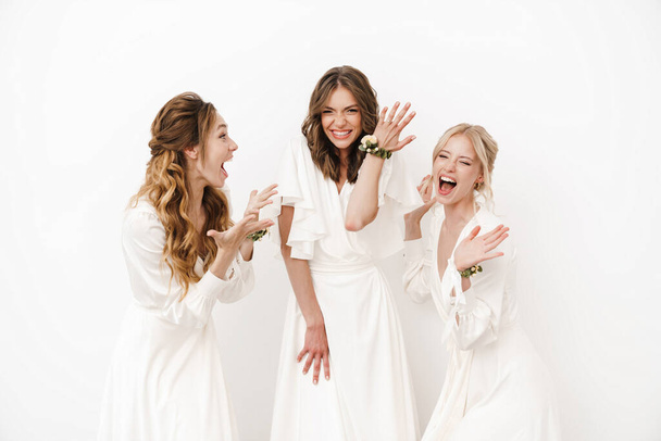 Photo of attractive happy bride showing her wedding ring at excited bridesmaids isolated over white wall - Foto, afbeelding