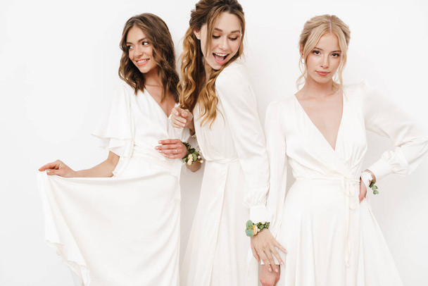 Photo of pleased beautiful bridesmaids in dresses posing on camera isolated over white wall - Fotoğraf, Görsel