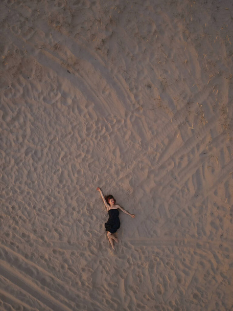 Young woman in a black dress lying on the back on the sand. Top view from the drone. Aerial Shooting. - Fotografie, Obrázek