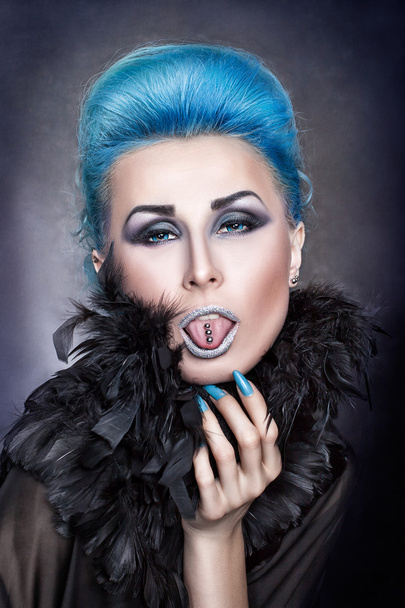 Дівчина з блакитним волоссям показує проколотий язик
. - Фото, зображення