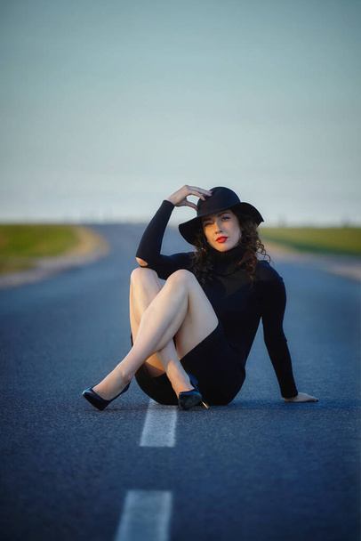 attractive girl in black dress and hat posing on the road with a dividing strip - Photo, Image