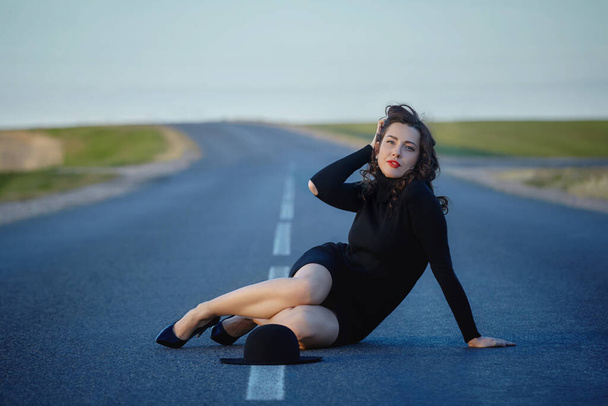 attractive girl in black dress and hat posing on the road with a dividing strip - Foto, Imagem