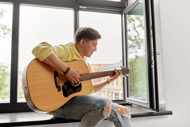 young man playing guitar sitting on windowsill - Foto, imagen