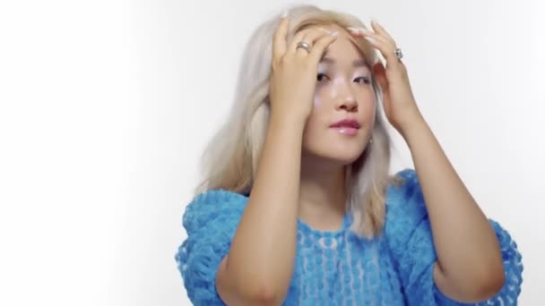 detailní portrét blondýny korejské modelky s lesklým make-upem sledující její nehty a dotýkající se jejích vlasů - Záběry, video