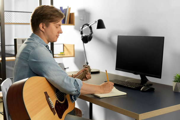 man with guitar writing to music book at home - Photo, image