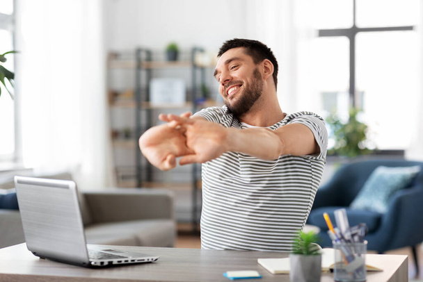 happy man with laptop stretching at home office - Photo, Image