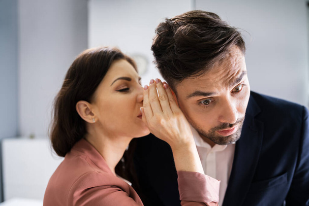 Woman Whispering Gossip In Friend's Ear At Workplace In Office - 写真・画像