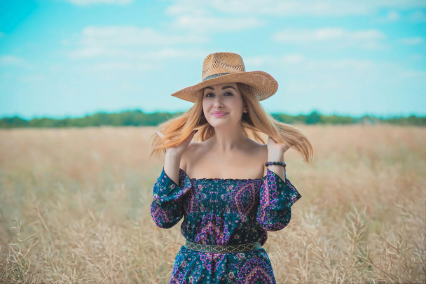 Egy nő a mezőn rusztikus szalmakalapot visel, boho pamut ruha, női divat - Fotó, kép