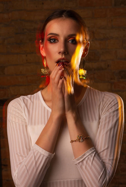 Plan studio d'une jeune femme merveilleuse avec un maquillage lumineux filmé dans une technique de lumière mixte au studio sombre - Photo, image