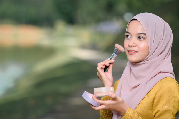 Asean woman applying makeup on her face, wearing traditional Malay  dress. - Photo, Image