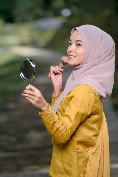 Asean woman applying makeup on her face, wearing traditional Malay  dress. - Photo, Image