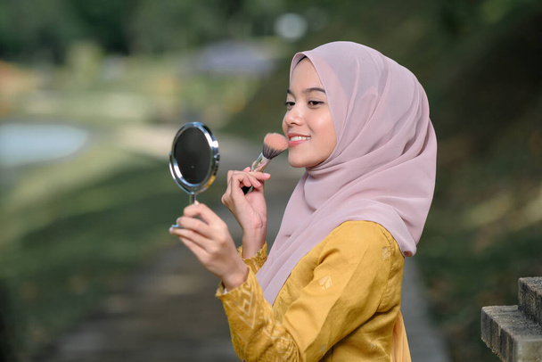 Aseanská žena nanáší make-up na obličej, nosí tradiční malajské šaty. - Fotografie, Obrázek
