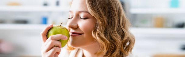cultivo panorámico de mujer con los ojos cerrados oliendo manzana - Foto, Imagen