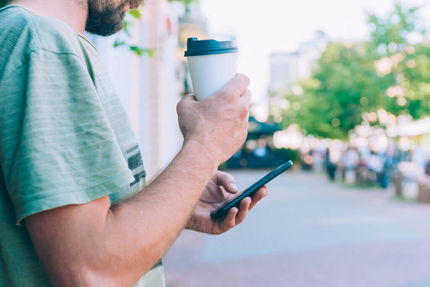 The guy drinks coffee from a plastic cup and holds a smartphone in his hand - Foto, Imagem