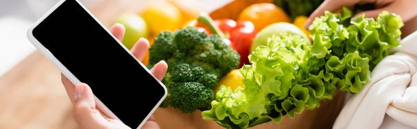 panoráma termés nő gazdaság okostelefon üres képernyő élelmiszerbolt közelében  - Fotó, kép