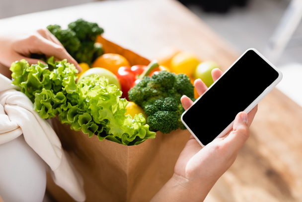 selective focus of woman holding smartphone with blank screen near groceries  - Foto, Imagen