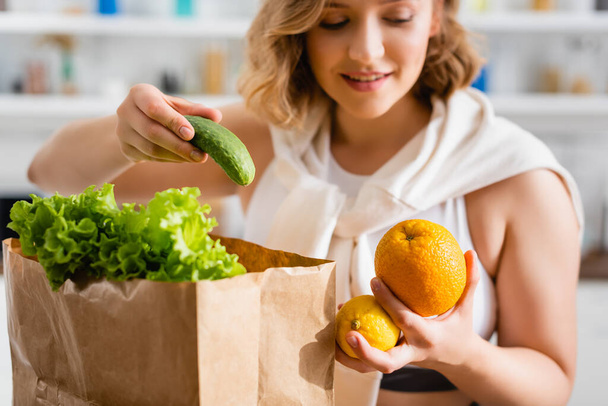selective focus of woman holding cucumber, lemon and orange near paper bag  - Φωτογραφία, εικόνα
