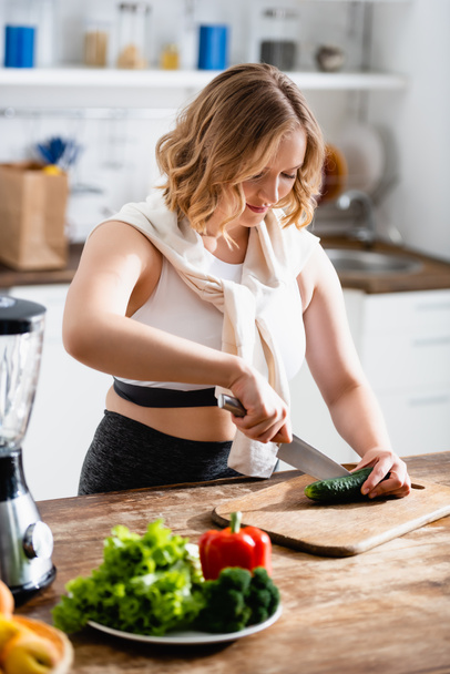 selective focus of young woman cutting cucumber on chopping board - Foto, afbeelding