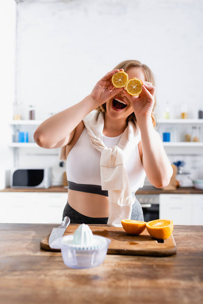 selective focus of woman covering eyes with halves of oranges near juicer  - Foto, Bild