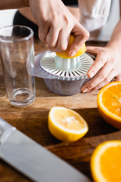cropped view of young woman squeezing half of orange in juicer - Foto, afbeelding