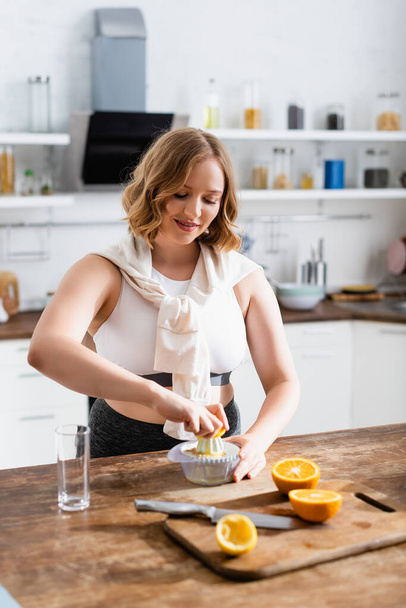 selective focus of young woman squeezing orange while preparing juice in kitchen  - Fotoğraf, Görsel