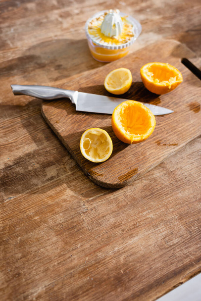 high angle view of squeezed orange halves near knife and juicer  - Foto, Imagem
