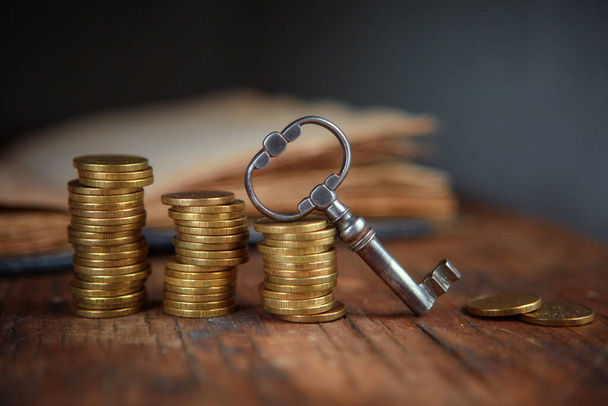 An old beautiful old key, a stack of gold coins, an old book. Business start-up, investment, treasure hunting, or the concept of the key to success - Valokuva, kuva