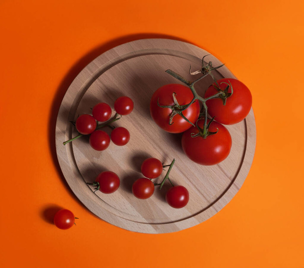 Food photography - Beautiful colorful still life with fresh summer vegetables of peppers, tomatoes and cherry tomatoes on a wooden board on an orange background - 写真・画像