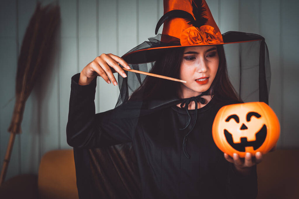 Attraktive schöne asiatische Frau als Hexe mit Jack-o-Laterne in der Hand verkleidet, Halloween-Feiertage im dunklen Ton des Kinos. - Foto, Bild