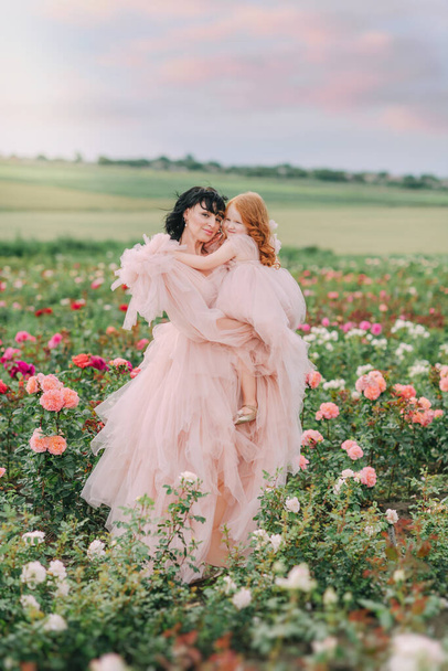 Mom and daughter in pink dresses on a field of roses - Photo, Image