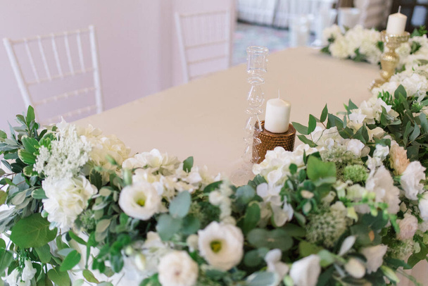 Wedding banquet table for newlyweds with flowers, greenery, white cloth and candles. Lush floral arrangement on wedding table. Luxury wedding decorations - Fotó, kép