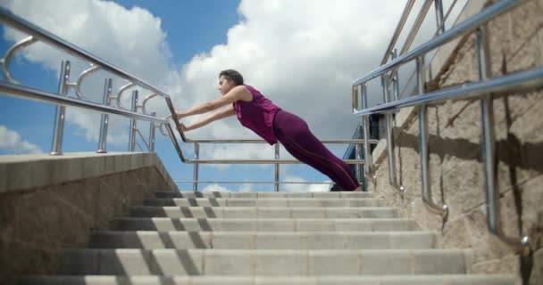 Atlétikai nő csinál nyújtás gyakorlatok a korlátok utcai lépcsők, fitness a városi környezetben, jóga osztály szabadban, fizikai edzés a városban, 4k 120p Prores HQ - Felvétel, videó
