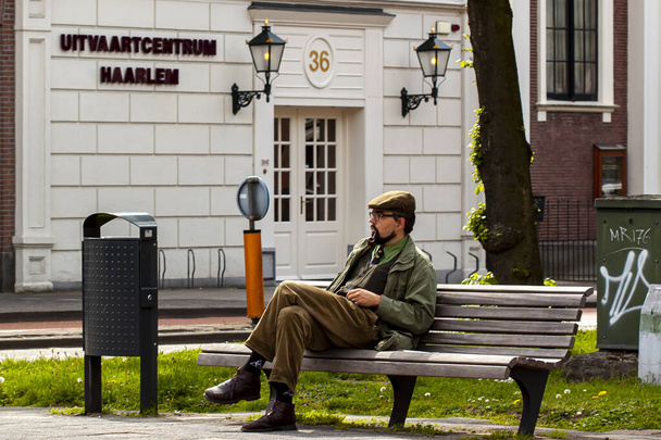 Haarlem, Netherlands 05/16/2010:  A young well dressed man wearing old style clothing is sitting crosslegged on a bench in front of a funeral home in Haarlem. He is alone and thinking. - Photo, Image